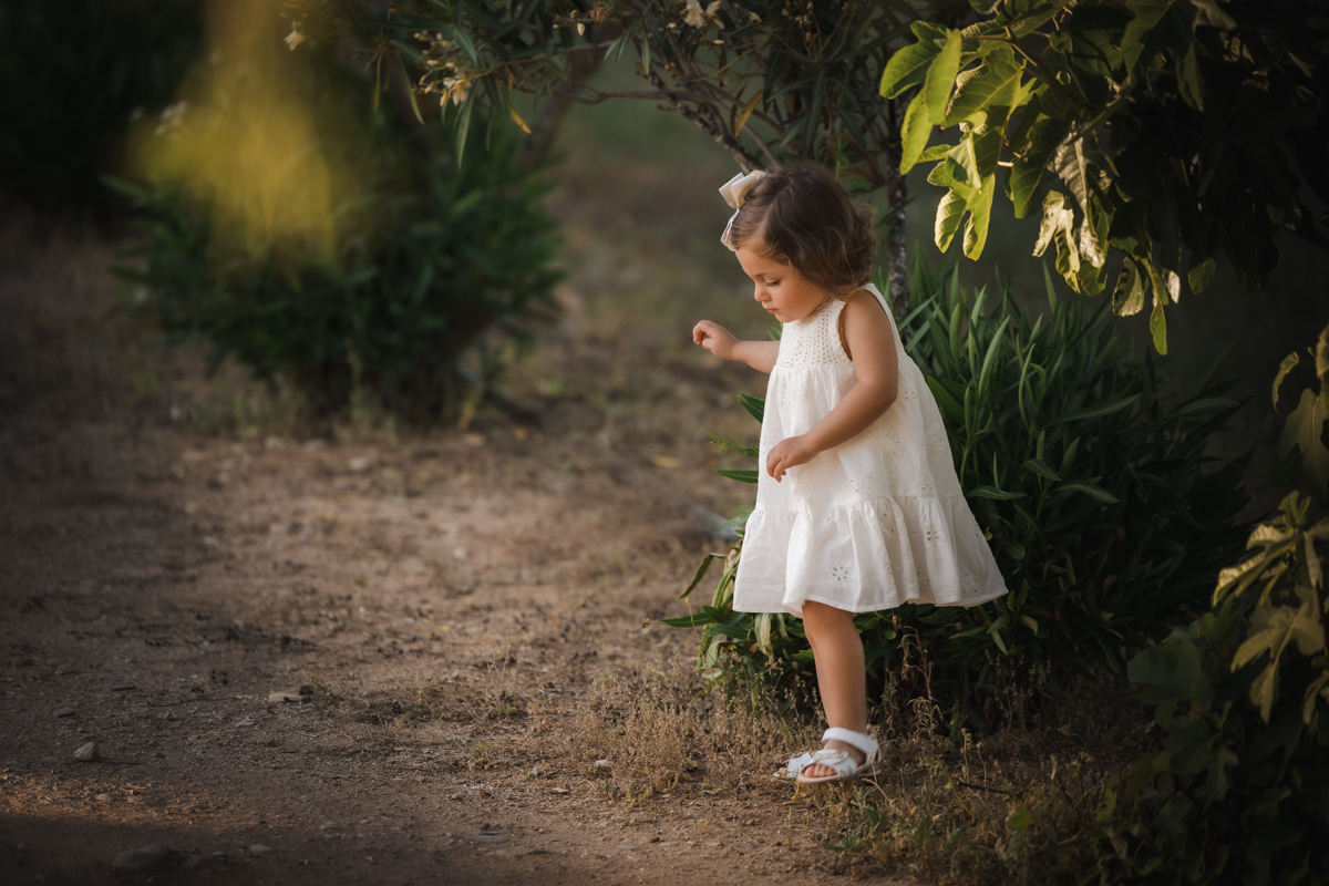 Niña de dos años con vestido blanco caminando por el campo
