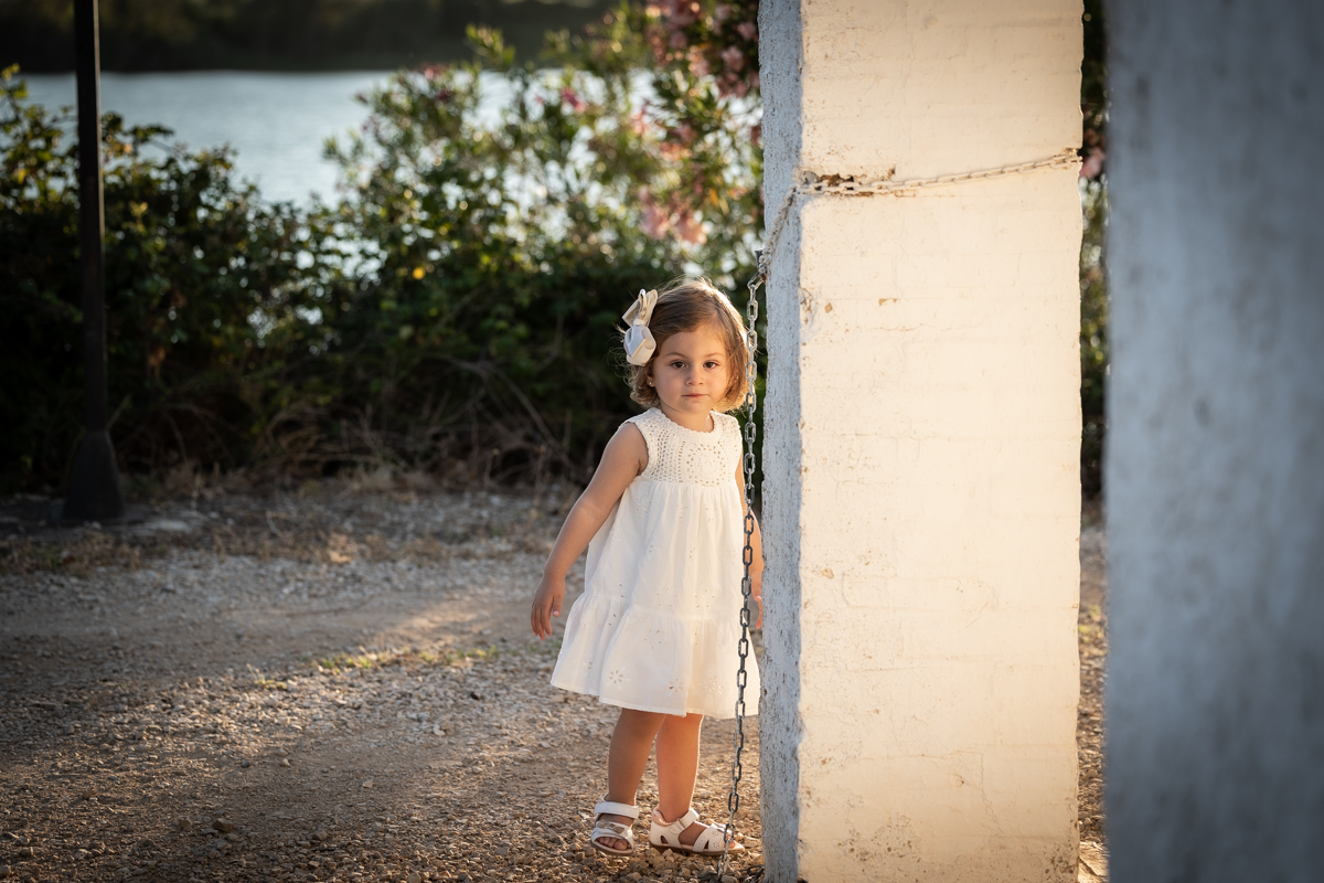 Niña de dos años de cuerpo entero, vestida de blanco, caminando junto a una casa de campo