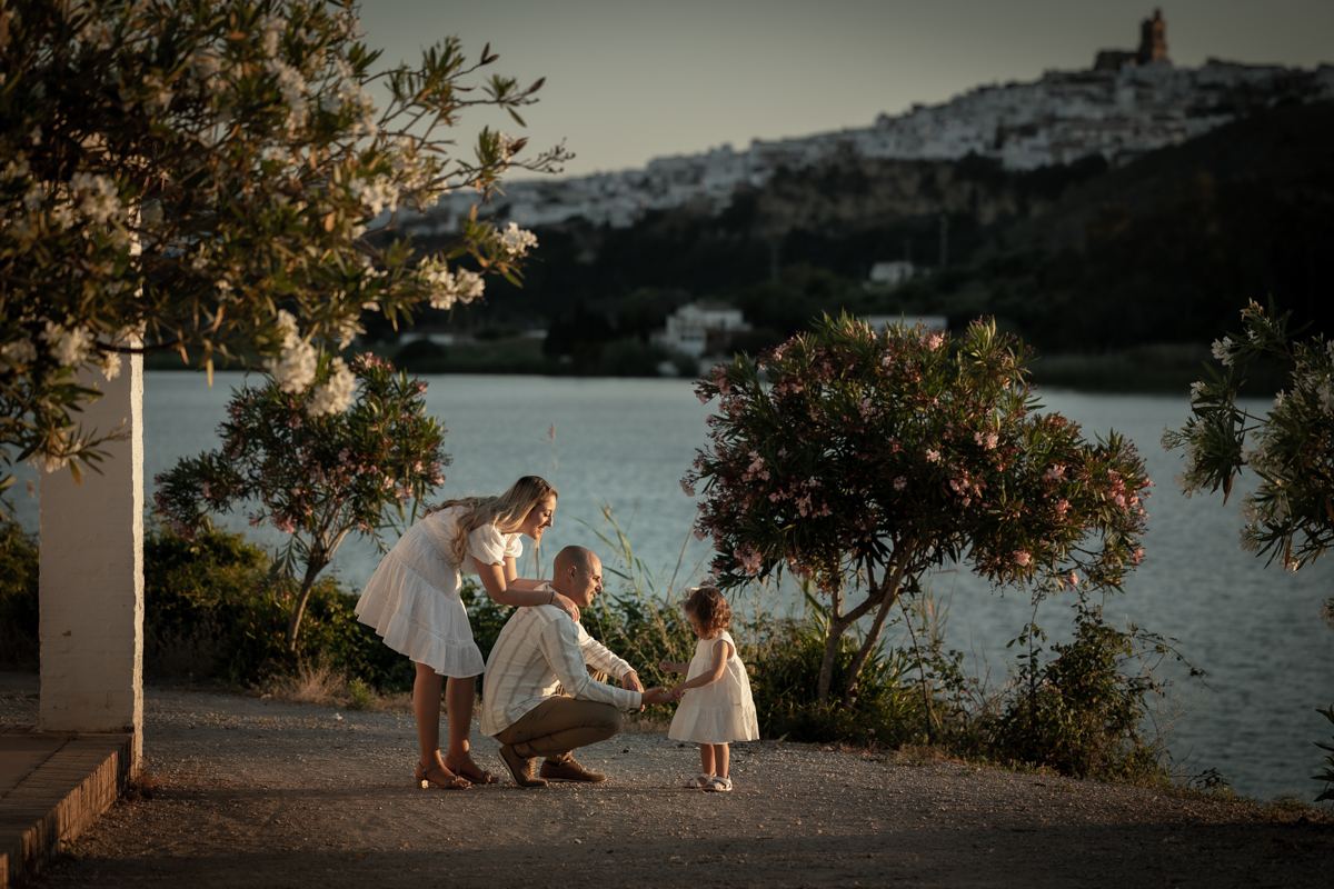 Mujer de mediana edad, de pelo rubio, vestido blanco, posa de cuerpo entero junto al lago de Arcos