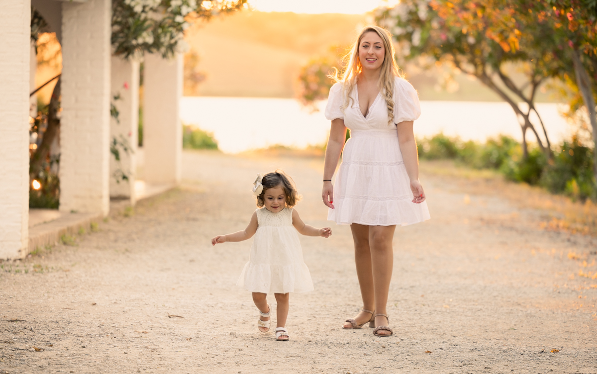 Madre de pelo rubio y vestida de blanco pasea con su hija pequeña por un camino rural