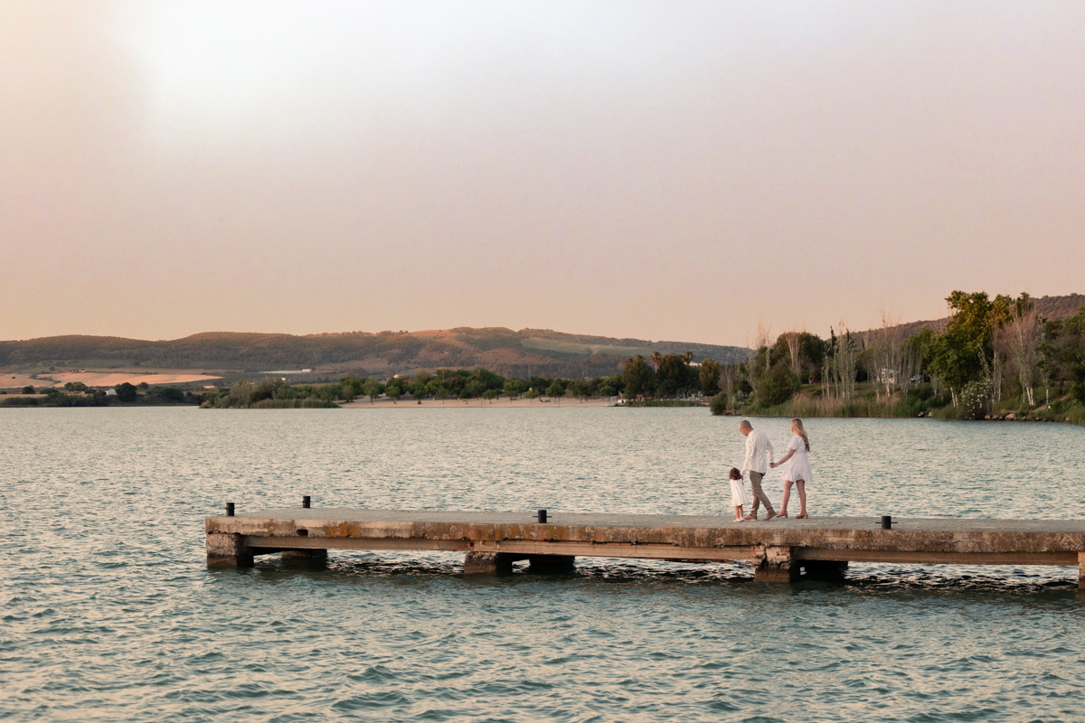Familia compuesta por una mujer, hombre y niña de dos años, caminan al atardecer junto al algo de Arcos