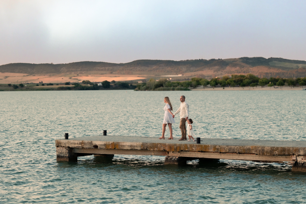 Familia compuesta por una mujer, hombre y niña de dos años, caminan al atardecer junto al algo de Arcos