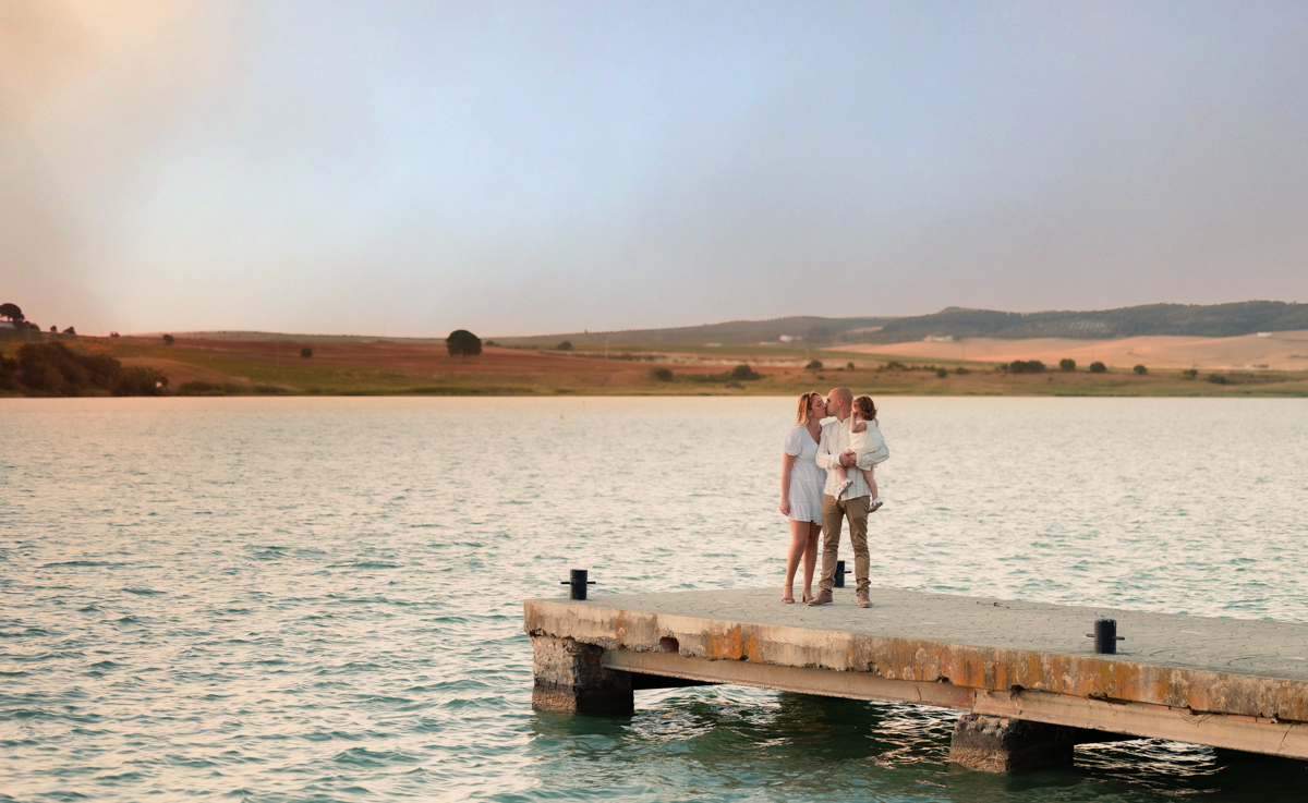 Familia compuesta por una mujer, hombre y niña de dos años, caminan al atardecer junto al algo de Arcos