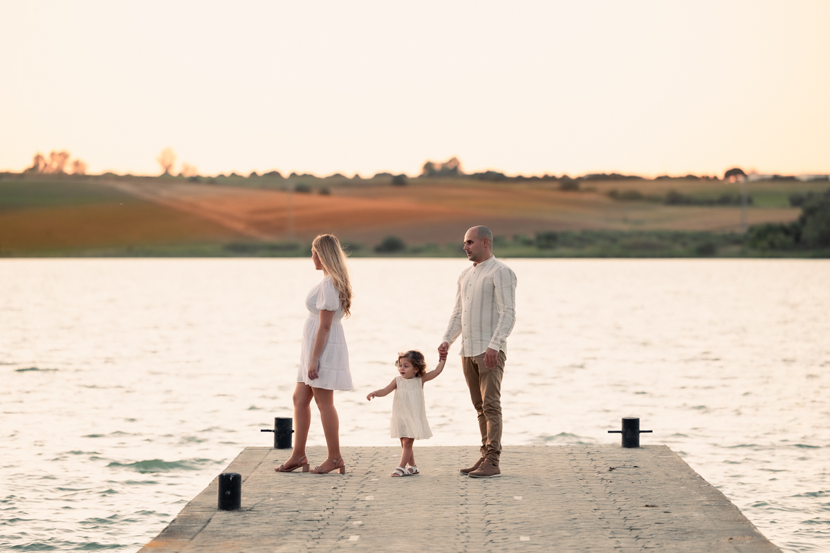 Familia compuesta por una mujer, hombre y niña de dos años, caminan al atardecer junto al algo de Arcos
