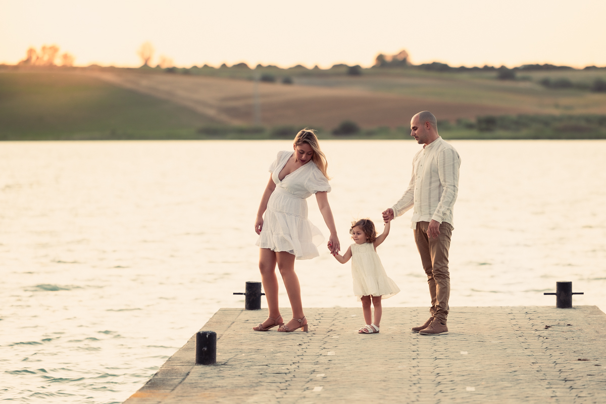 Familia compuesta por una mujer, hombre y niña de dos años, caminan al atardecer junto al algo de Arcos