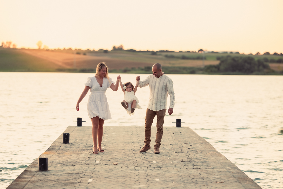 Familia compuesta por una mujer, hombre y niña de dos años, caminan al atardecer junto al algo de Arcos
