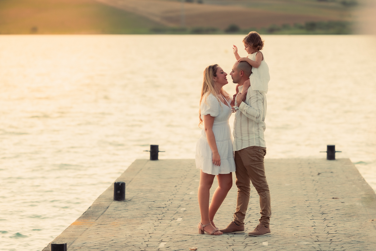 Familia compuesta por una mujer, hombre y niña de dos años, caminan al atardecer junto al algo de Arcos