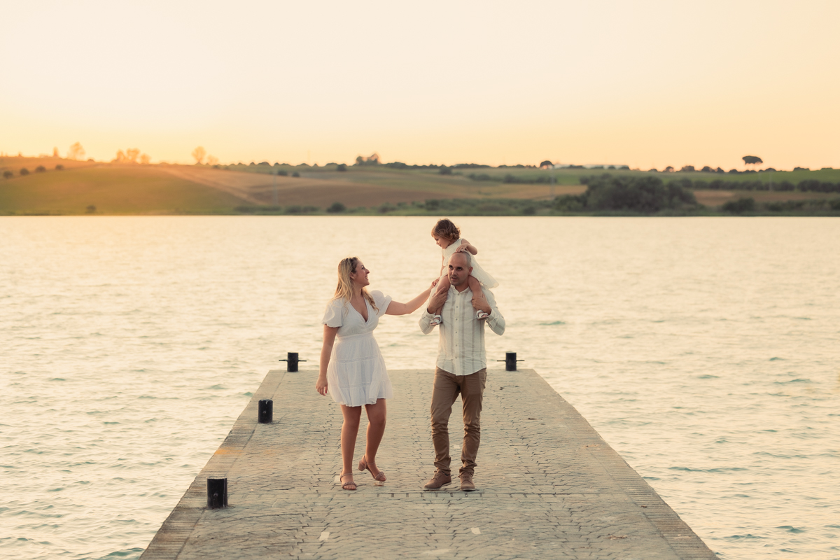 Familia compuesta por una mujer, hombre y niña de dos años, caminan al atardecer junto al algo de Arcos