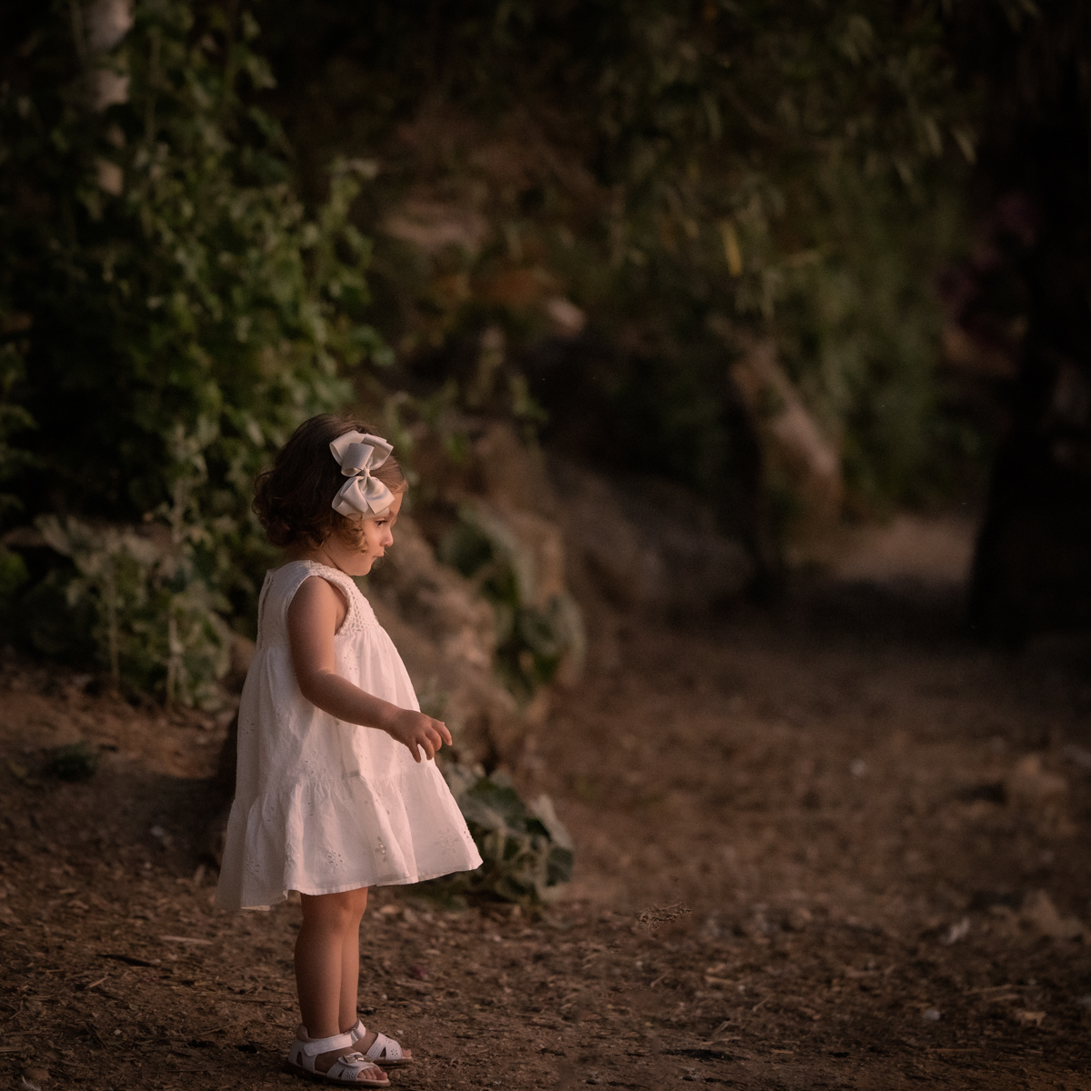 Niña pequeña vestida de blanco juega con unos patos junto al lago de Arcos