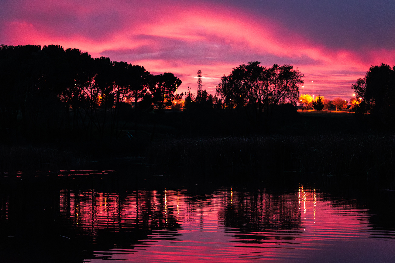 Anochecer rojizo en lago con industria de fondo